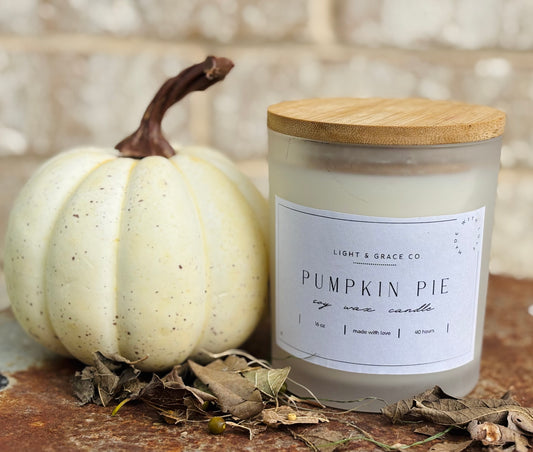 Pumpkin pie candle with a wooden lid next to a white pumpkin on a wooden surface.